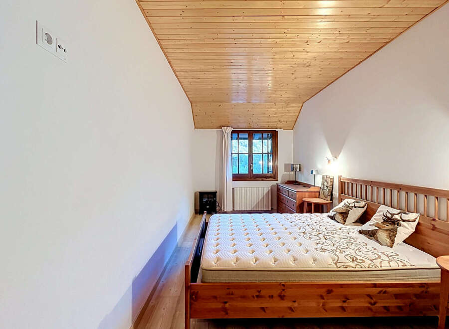 Experience cozy mountain living in this charming bedroom featuring a rustic wooden bed and a sloped, wood-paneled ceiling.
