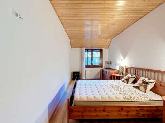 Experience cozy mountain living in this charming bedroom featuring a rustic wooden bed and a sloped, wood-paneled ceiling.