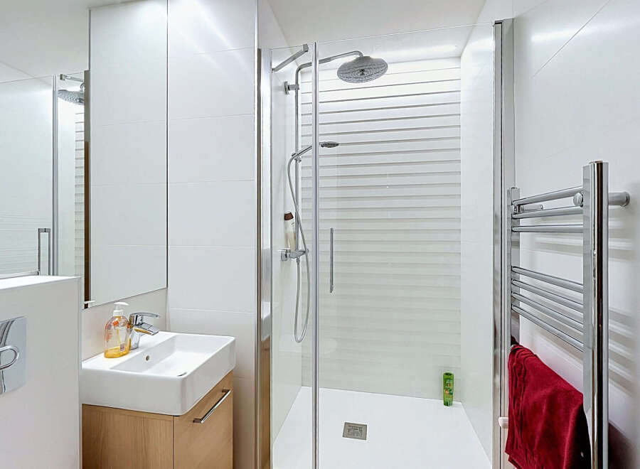 This modern bathroom features a sleek, minimalist design with white tiled walls and a spacious walk-in shower.