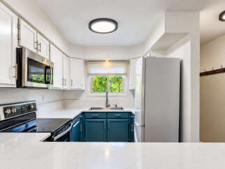 This modern kitchen features sleek white cabinetry complemented by striking teal lower cabinets, creating a vibrant and stylish cooking space.