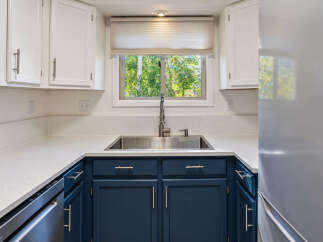 This modern kitchen features a deep stainless steel sink beneath a large window offering a view of lush greenery.