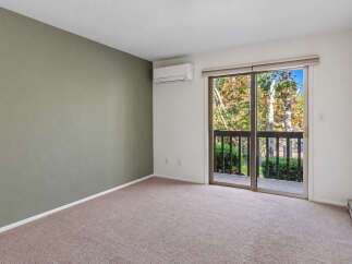 This spacious room features a calming sage green accent wall and a large sliding glass door that opens to a private balcony with scenic views of autumn foliage.