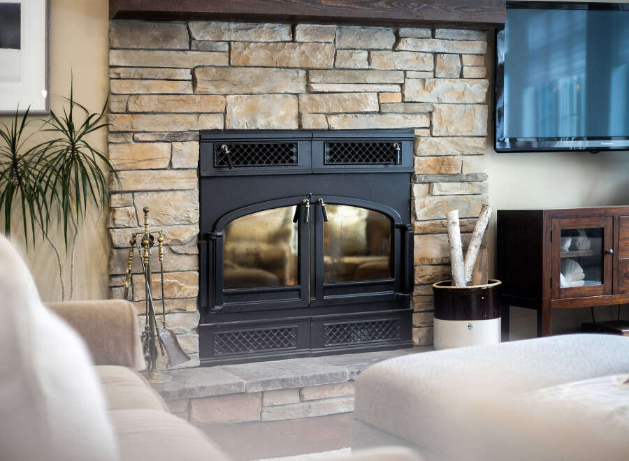 Experience cozy evenings by this stunning stone fireplace, featuring a black metal insert with glass doors and decorative grates.