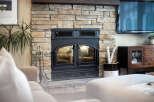 Experience cozy evenings by this stunning stone fireplace, featuring a black metal insert with glass doors and decorative grates.