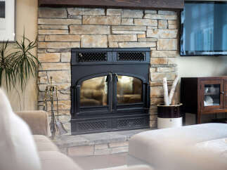 Experience cozy evenings by this stunning stone fireplace, featuring a black metal insert with glass doors and decorative grates.