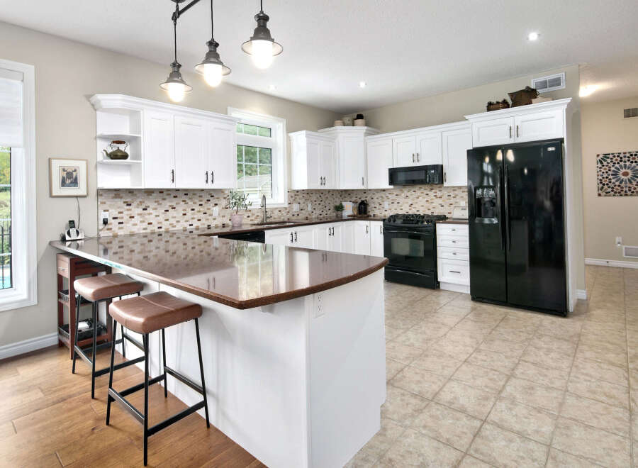 This spacious kitchen features white shaker cabinets, a multi-colored tile backsplash, and a large granite island with seating.