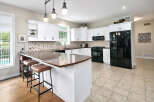 This spacious kitchen features white shaker cabinets, a multi-colored tile backsplash, and a large granite island with seating.