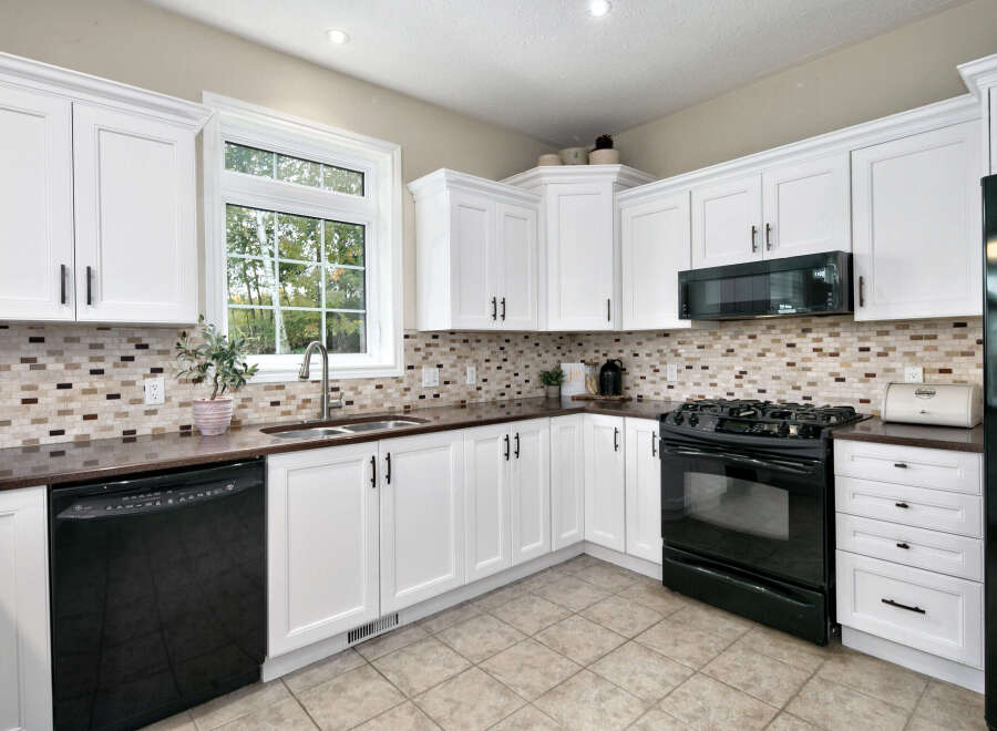 This kitchen boasts bright white cabinetry with dark hardware, complemented by a stylish mosaic tile backsplash.
