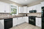 This kitchen boasts bright white cabinetry with dark hardware, complemented by a stylish mosaic tile backsplash.