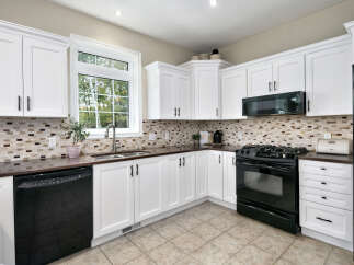 This kitchen boasts bright white cabinetry with dark hardware, complemented by a stylish mosaic tile backsplash.
