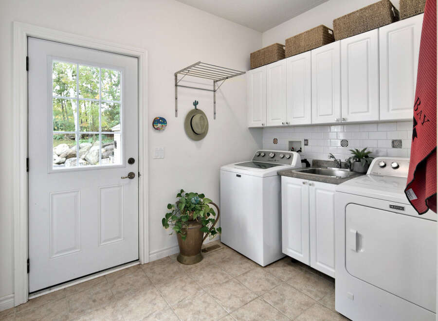 This laundry room features a white Maytag washer and dryer set, complemented by white cabinetry and a subway tile backsplash.