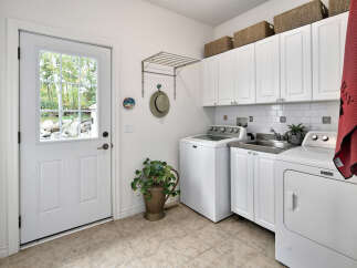 This laundry room features a white Maytag washer and dryer set, complemented by white cabinetry and a subway tile backsplash.