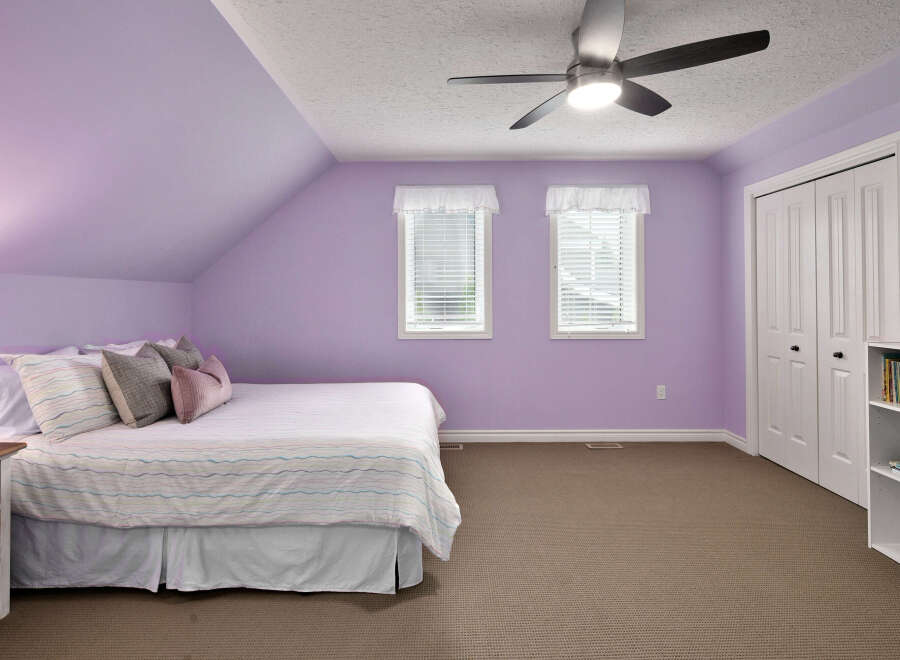 This charming bedroom features a comfortable bed with a striped comforter and decorative pillows, set against soothing lavender walls.