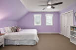 This charming bedroom features a comfortable bed with a striped comforter and decorative pillows, set against soothing lavender walls.