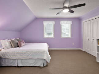 This charming bedroom features a comfortable bed with a striped comforter and decorative pillows, set against soothing lavender walls.