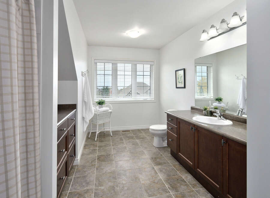 This spacious bathroom features a large vanity with ample storage, a comfortable toilet, and a bright window with blinds.