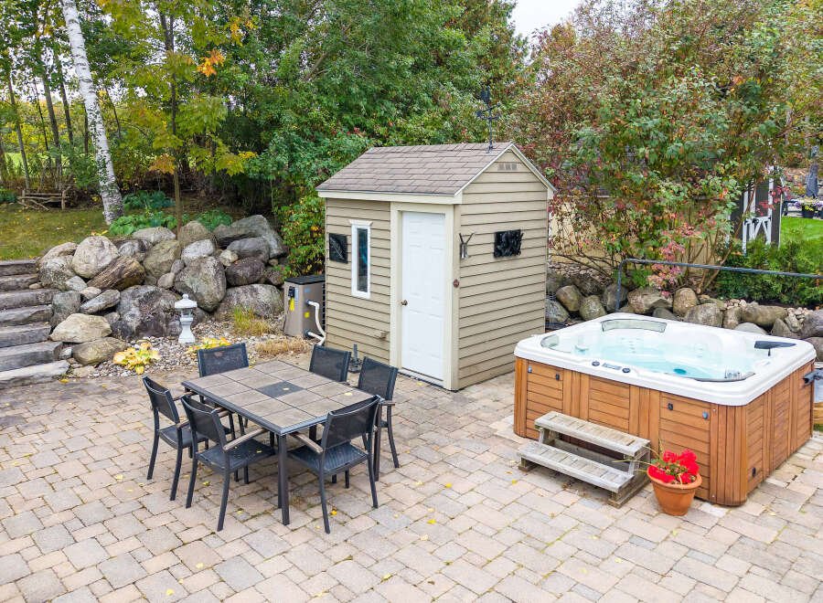 Enjoy outdoor living with this spacious patio featuring a dining set and a luxurious hot tub, perfect for relaxation and entertaining.