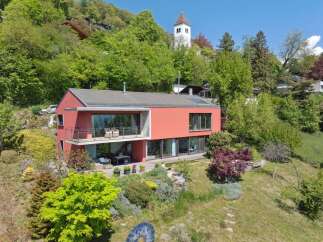 Experience modern living in this stunning red villa, nestled on a lush green hillside with breathtaking views.