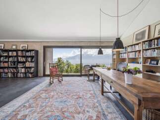 Experience breathtaking mountain and lake views from this stunning home office, featuring a large wooden desk and ample bookshelves.