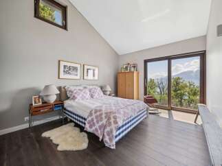 Experience breathtaking mountain views from this serene bedroom, featuring a comfortable bed adorned with a charming floral duvet and a classic blue and white checkered bed skirt.