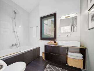 This modern bathroom features a sleek white bathtub with a dark wood surround, complemented by a minimalist vanity with a rectangular vessel sink.