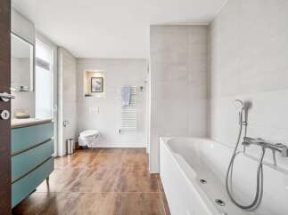 Experience modern luxury in this spacious bathroom, featuring a sleek white bathtub with a handheld showerhead and chrome fixtures.