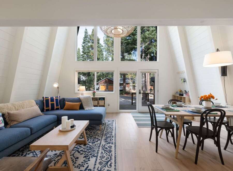 Experience the charm of this A-frame cabin, featuring a spacious living area with a large sectional sofa and a cozy coffee table.