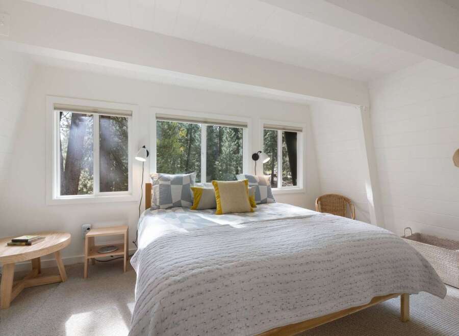Experience serene living in this charming bedroom, bathed in natural light from large windows overlooking a lush forest.