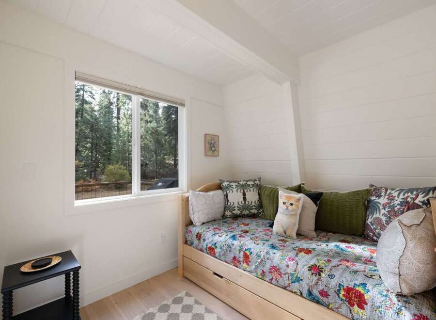 Experience serene living with this charming bedroom featuring a comfortable daybed adorned with a vibrant floral quilt and an adorable cat pillow.