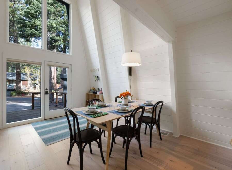 Experience the charm of this A-frame dining area, bathed in natural light from expansive windows overlooking a serene wooded landscape.