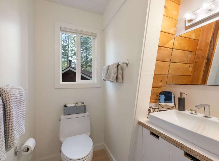 This bright and airy bathroom features a modern white vanity with a sleek faucet, complemented by warm wooden accents on the wall.