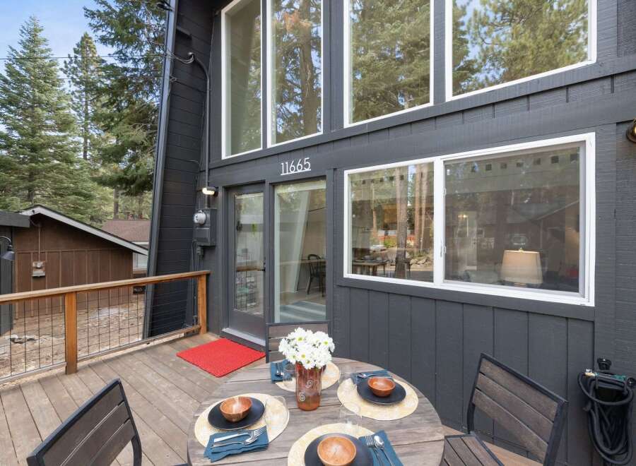 Enjoy outdoor dining on this charming wooden deck, complete with a round table set for four and a vibrant red accent rug.