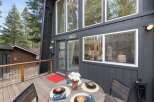 Enjoy outdoor dining on this charming wooden deck, complete with a round table set for four and a vibrant red accent rug.