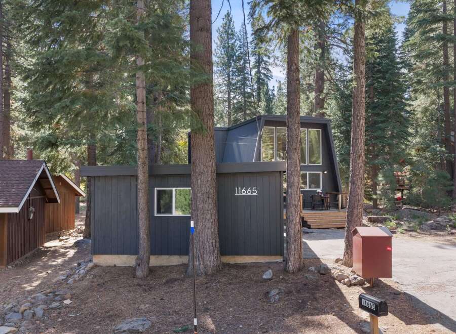 Nestled amongst tall pine trees, this modern A-frame home offers a unique architectural design with a dark exterior and large windows.