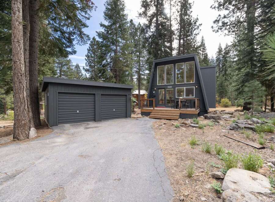 Discover this modern A-frame home nestled among tall pine trees, featuring a striking dark exterior and expansive windows.