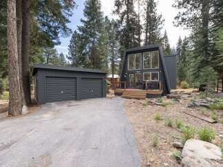 Discover this modern A-frame home nestled among tall pine trees, featuring a striking dark exterior and expansive windows.