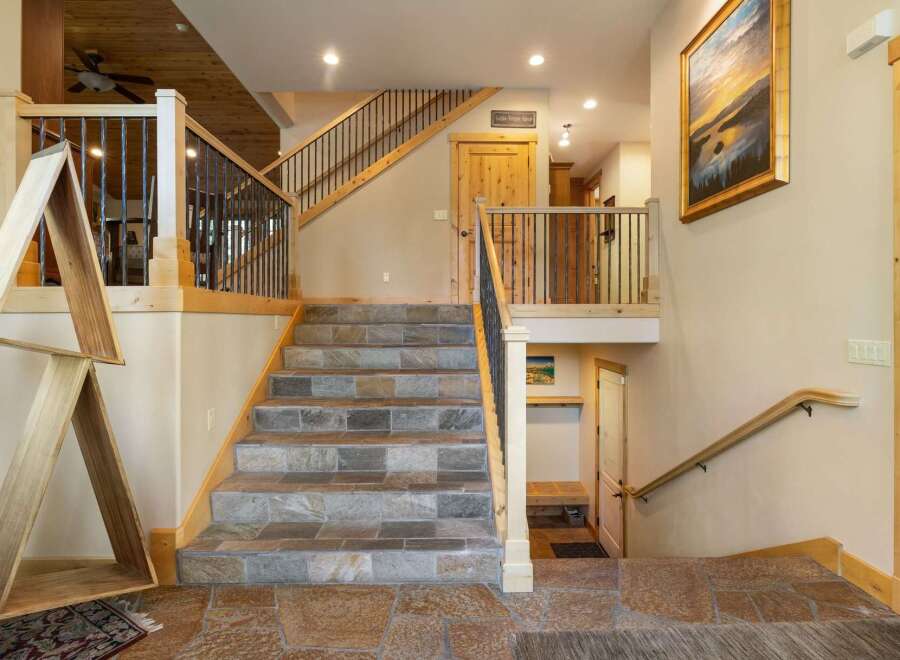 This stunning home features a grand staircase with slate tile risers and treads, complemented by a rustic wooden handrail and black metal balusters.