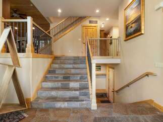 This stunning home features a grand staircase with slate tile risers and treads, complemented by a rustic wooden handrail and black metal balusters.