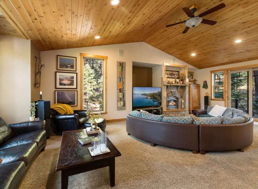Experience rustic charm in this spacious living room, featuring a vaulted wood-paneled ceiling and a cozy stone fireplace.