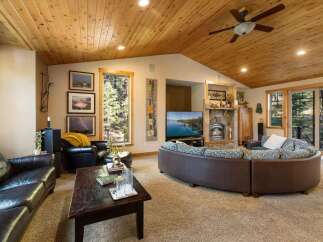 Experience rustic charm in this spacious living room, featuring a vaulted wood-paneled ceiling and a cozy stone fireplace.