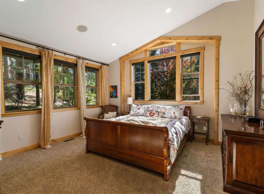 Experience serene living in this charming bedroom, featuring a beautiful wooden sleigh bed and large windows that offer picturesque views of the surrounding trees.