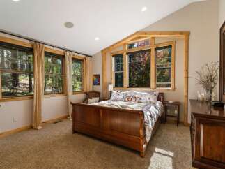 Experience serene living in this charming bedroom, featuring a beautiful wooden sleigh bed and large windows that offer picturesque views of the surrounding trees.