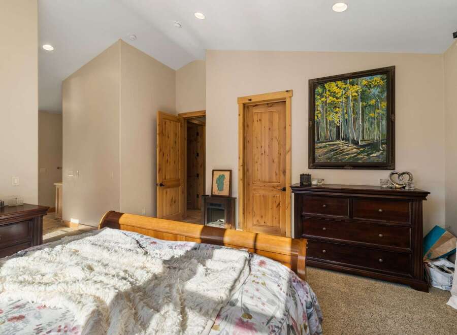 This inviting bedroom features a cozy sleigh bed with plush bedding, complemented by a dark wood dresser adorned with a beautiful forest landscape painting.
