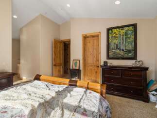 This inviting bedroom features a cozy sleigh bed with plush bedding, complemented by a dark wood dresser adorned with a beautiful forest landscape painting.