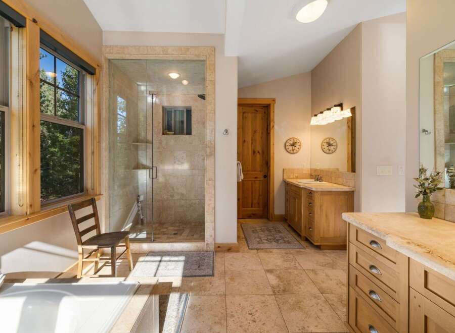 Experience luxury in this spacious bathroom featuring a large, walk-in glass shower with travertine tile and a separate soaking tub.
