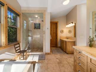 Experience luxury in this spacious bathroom featuring a large, walk-in glass shower with travertine tile and a separate soaking tub.