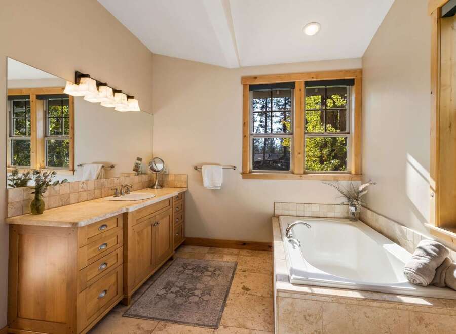 This spacious bathroom features a large soaking tub with a view of the surrounding trees through the wooden-framed window.
