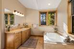 This spacious bathroom features a large soaking tub with a view of the surrounding trees through the wooden-framed window.