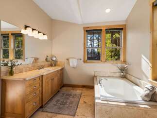 This spacious bathroom features a large soaking tub with a view of the surrounding trees through the wooden-framed window.