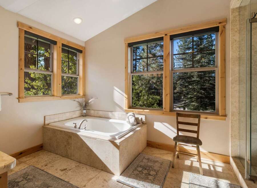Indulge in relaxation in this luxurious bathroom, featuring a spacious soaking tub perfectly positioned to offer serene views of the surrounding pine forest through large windows.